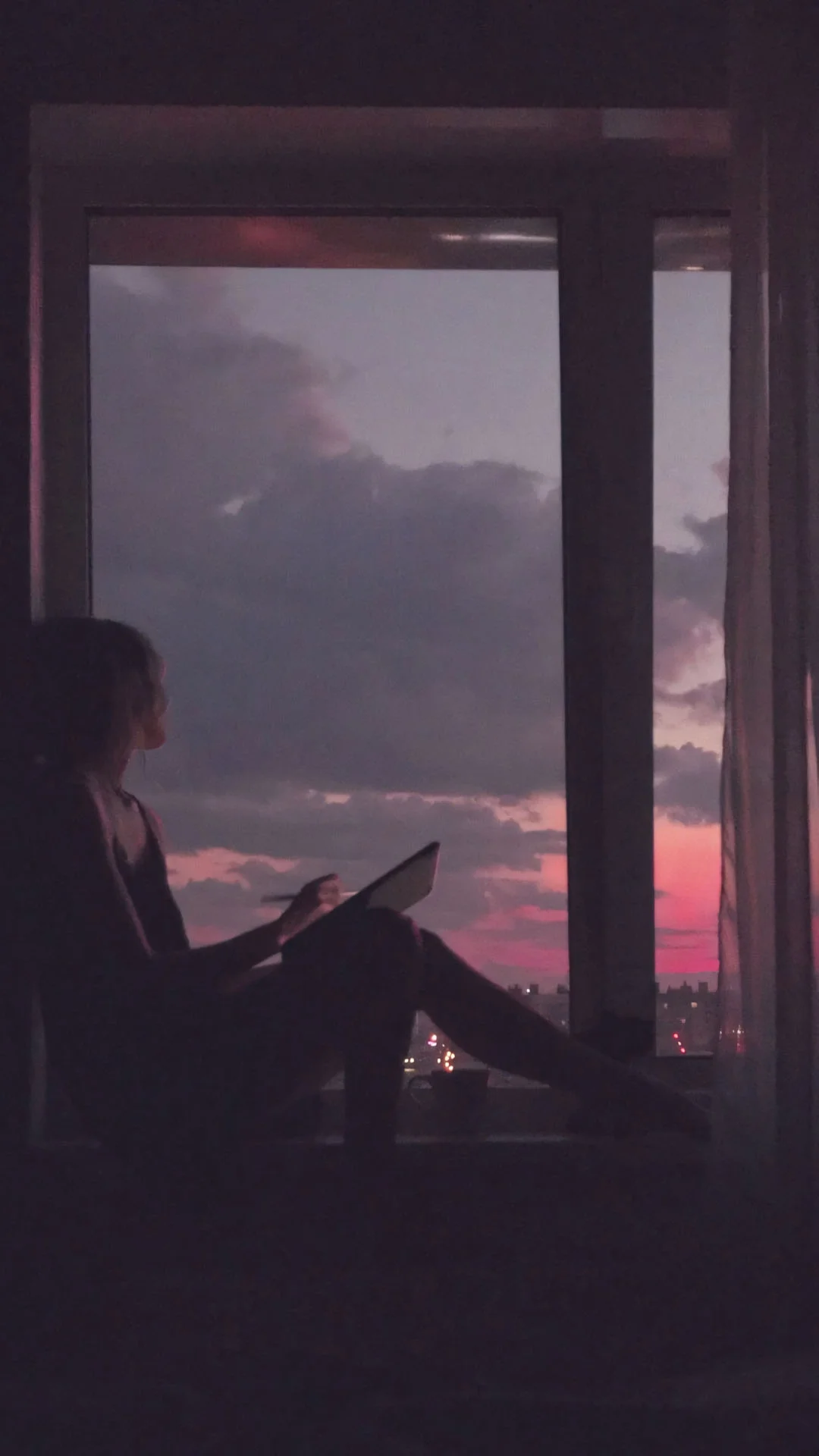 người phụ nữ ngồi bên cửa sổ ngắm bầu trời hoàng hôn