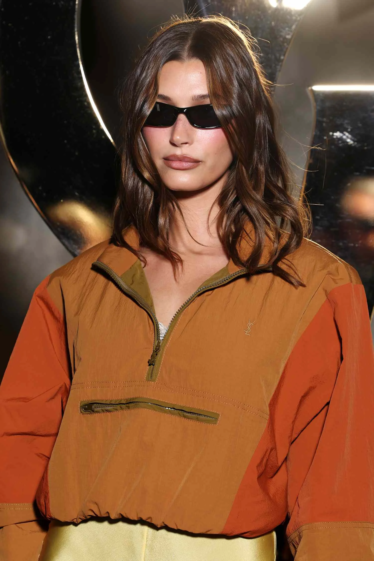 Hailey Bieber in dark sunglasses and an earth-toned windbreaker